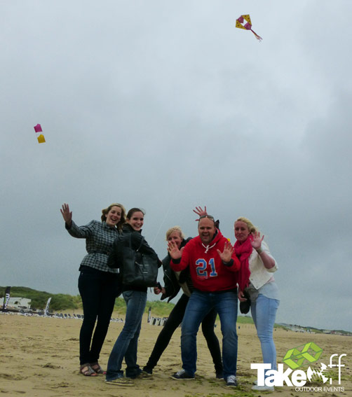 Vrolijke team mensen op het strand met hun vlieger succesvol in de lucht.